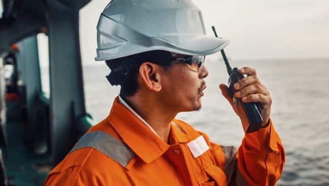 Officier de pont philippin sur le pont d'un navire ou d'un navire, portant un équipement de protection individuelle EPI.  Il parle à la radio talkie-walkie VHF dans les mains.  Travail de rêve en mer