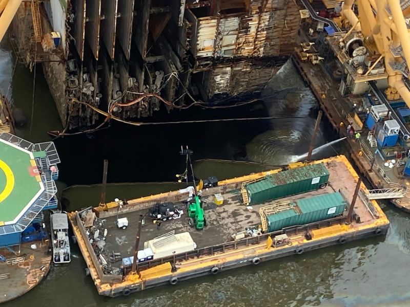 Une équipe de récupération du pétrole utilise un aspirateur flottant connecté à des conteneurs verts pour pomper le pétrole